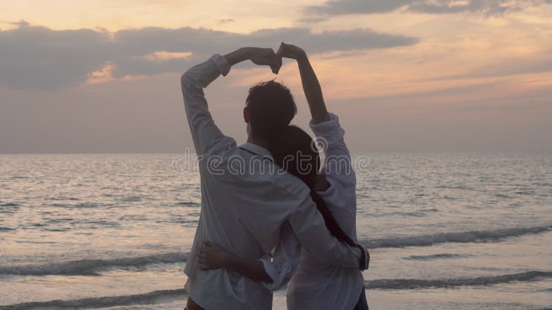 Silhouet van het gelukkige aziatische paar houdt van het gebaar hartvormig symbool van de hand op het strand in vakantie met roman