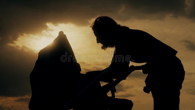 Silhouet van jonge moeder met een babywandelwagen die van moederschap genieten bij zonsondergang Jonge vrouw die kind in baby bek