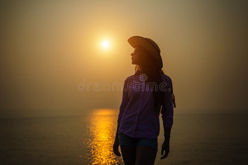 Silhouet van jonge vrouw in een hoed tegen zonsondergang over het overzees Het mooie slanke meisje geniet van vrede en ontspannin royalty-vrije stock afbeelding Silhouet van jonge vrouw in een hoed tegen zonsondergang over het overzees Het mooie slanke meisje geniet van vrede en ontspannin royalty-vrije stock afbeelding