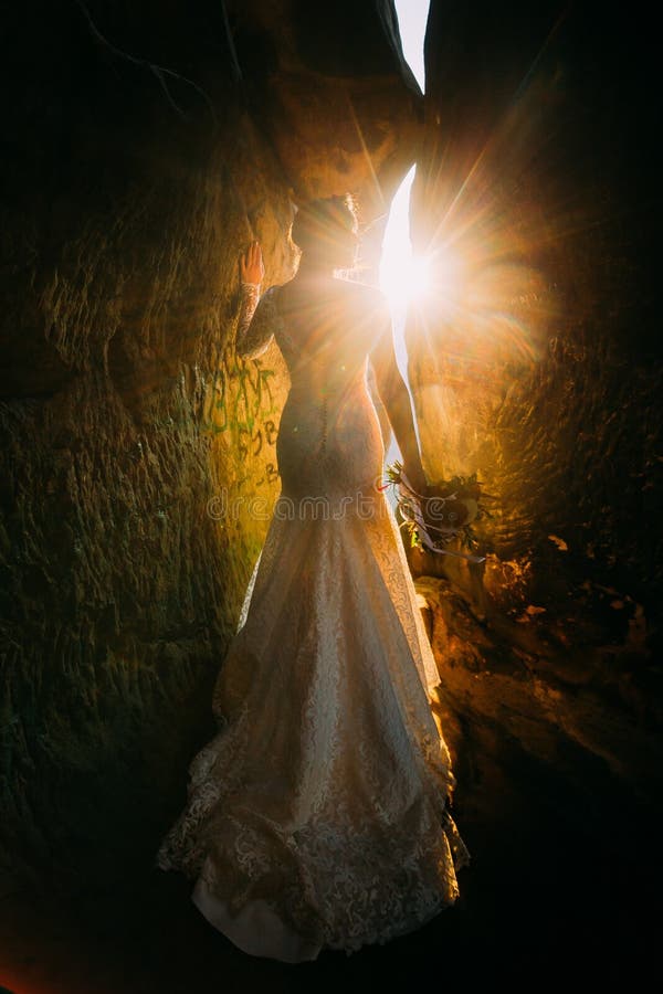 Silhouet van mooie jonge vrouw die elegante witte kleding dragen die zich tussen twee rotsen met gele zonsondergangstralen bevind royalty-vrije stock afbeeldingen Silhouet van mooie jonge vrouw die elegante witte kleding dragen die zich tussen twee rotsen met gele zonsondergangstralen bevind royalty-vrije stock afbeeldingen