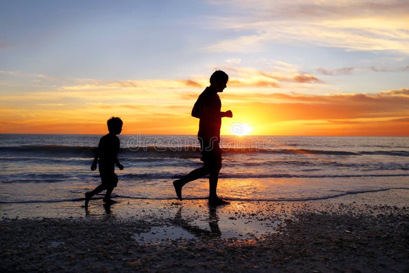 Silhouet van Vader en zijn Jonge Zoonsjogging op Strand samen bij Zonsondergang stock afbeeldingen Silhouet van Vader en zijn Jonge Zoonsjogging op Strand samen bij Zonsondergang stock afbeeldingen