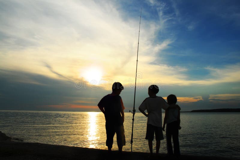 Silhouette of kids with fishing rod at sunset