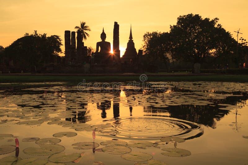 Silueta staroveké sochy Budhu a pagody proti západu slnka na oblohe v Sukhothai Historický Park, v Thajsku.