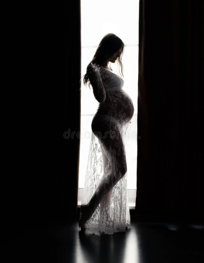 Silhouette of a beautiful pregnant woman near the window