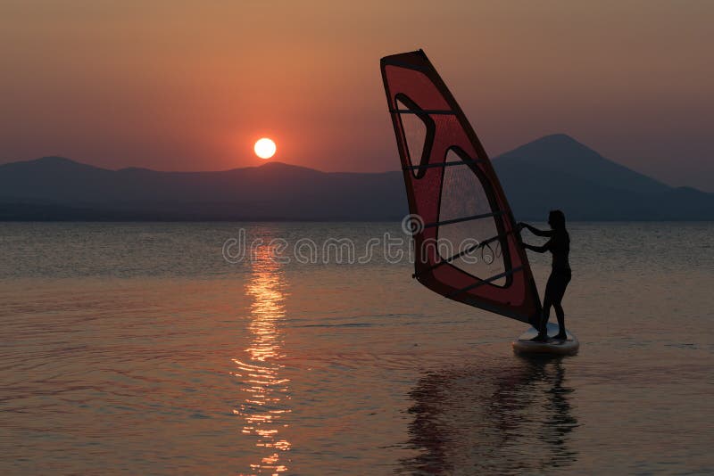 Silhouette of a beautiful woman surfing with her windsurf against the sun.