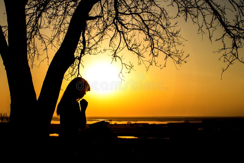 Silhouette of woman praying to God in the nature witth the Bible at sunset, the concept of religion and spirituality
