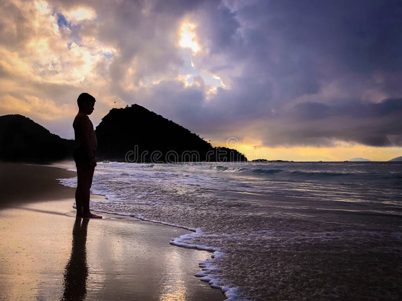 Silhouette of a boy standing on a shore with receding ocean waters