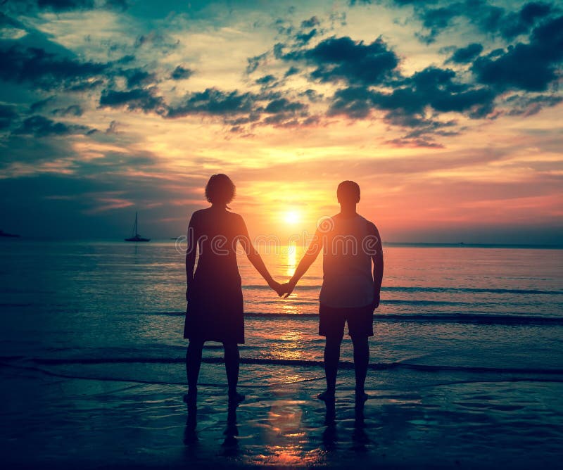 Silhouette of couple holding hands on the sea beach