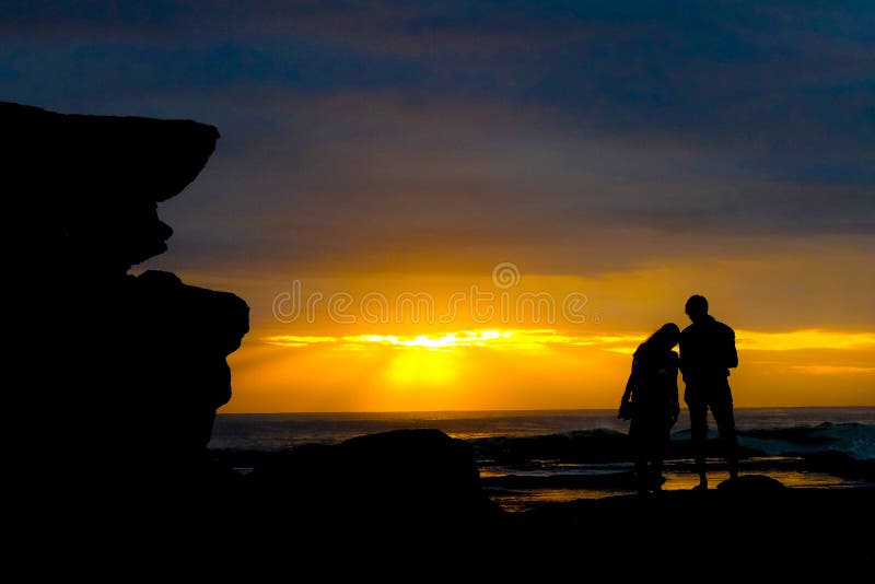 Silhouette of a couple looking at a georgous romantic sunset at the pacific ocean stock image Silhouette of a couple looking at a georgous romantic sunset at the pacific ocean stock image