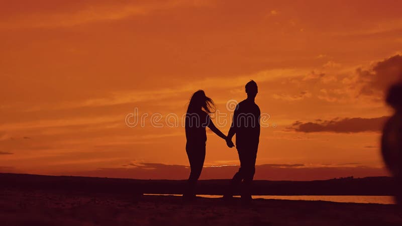 Silhouette of couple walking on beach at sunset holding hands. happy man and girl on seashore in the lights of sunset