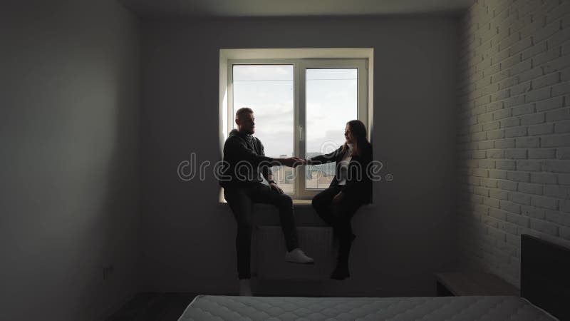 Silhouette d'un couple tendant la main vers l'autre en étant assis près de la fenêtre un couple tenant la main dans un clips vidéos