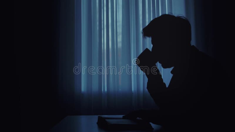 Silhouette d'un homme lisant par une fenêtre avec des rideaux banque de vidéos