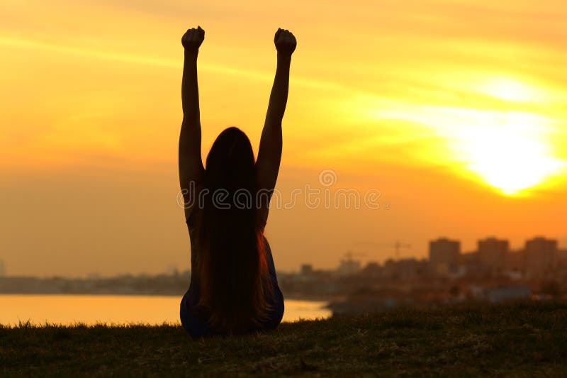 Silhouette d'une femme célébrant la levée des armes au coucher du soleil photographie stock