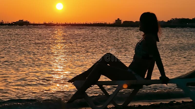 Silhouette d'une femme sur fond de lever de soleil coloré. la femme assise en bord de mer profite de la beauté du lever du soleil clips vidéos