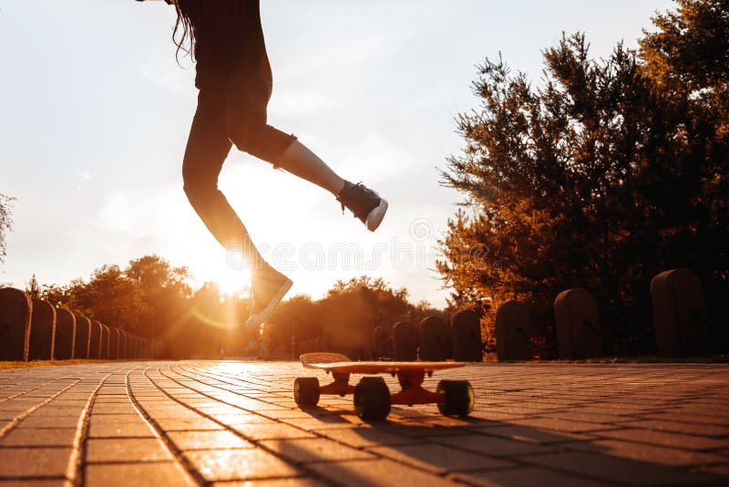 Silhouette d'une jeune fille de saut sur une planche à roulettes dans le coucher de soleil dans le parc photos libres de droits