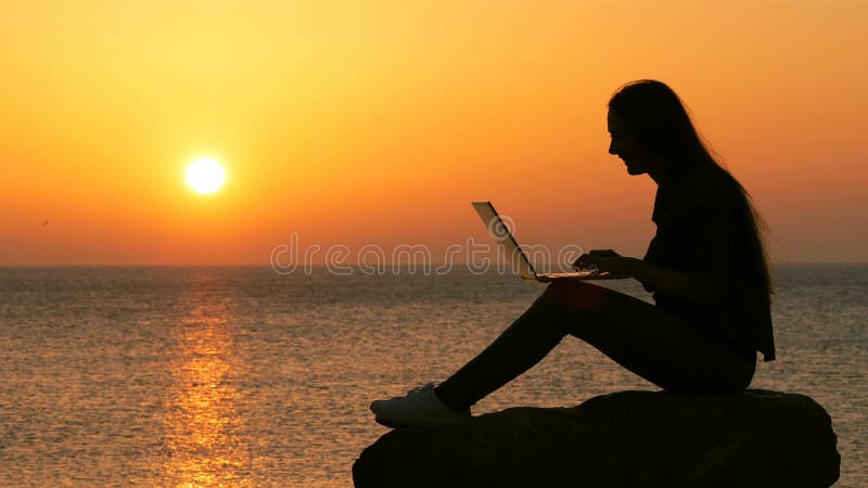 Silhouette de femme utilisant l'ordinateur portable au coucher du soleil banque de vidéos