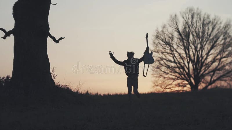 Silhouette de guitariste au mouvement lent de coucher du soleil courses avec une guitare dans des ses mains