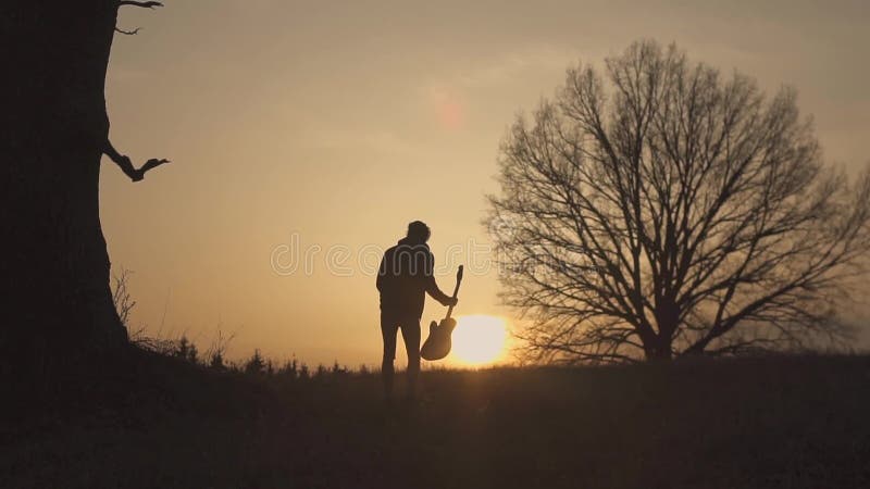 Silhouette de guitariste au mouvement lent de coucher du soleil ondulation de sa guitare et main