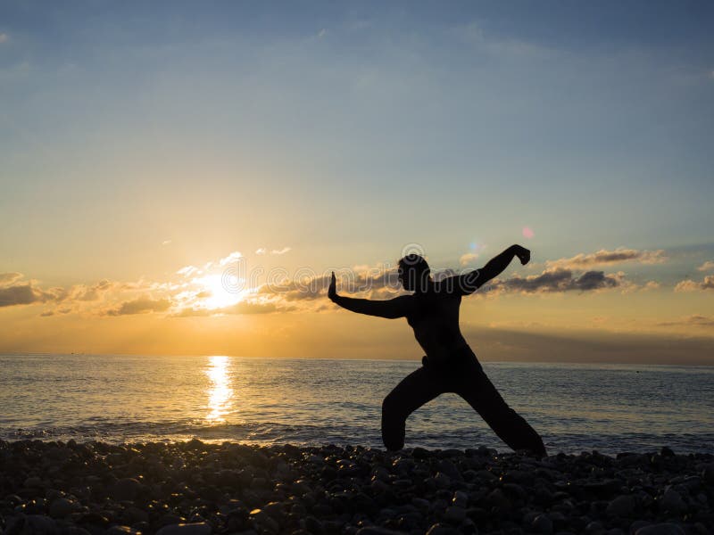 Silhouette de jeune artiste ou spécialiste martial masculin en yoga à la plage pendant le coucher du soleil spectaculaire images libres de droits Silhouette de jeune artiste ou spécialiste martial masculin en yoga à la plage pendant le coucher du soleil spectaculaire images libres de droits