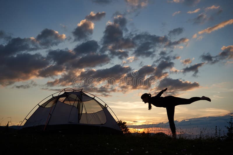 Silhouette de jeune femme s'étendant sur des montagnes au coucher du soleil près du camping contre le beau ciel images libres de droits Silhouette de jeune femme s'étendant sur des montagnes au coucher du soleil près du camping contre le beau ciel images libres de droits