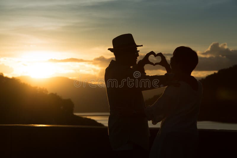 Silhouette de l'image des couples supérieurs romantiques heureux rendant la forme de coeur avec des mains extérieure au fond de c photos libres de droits