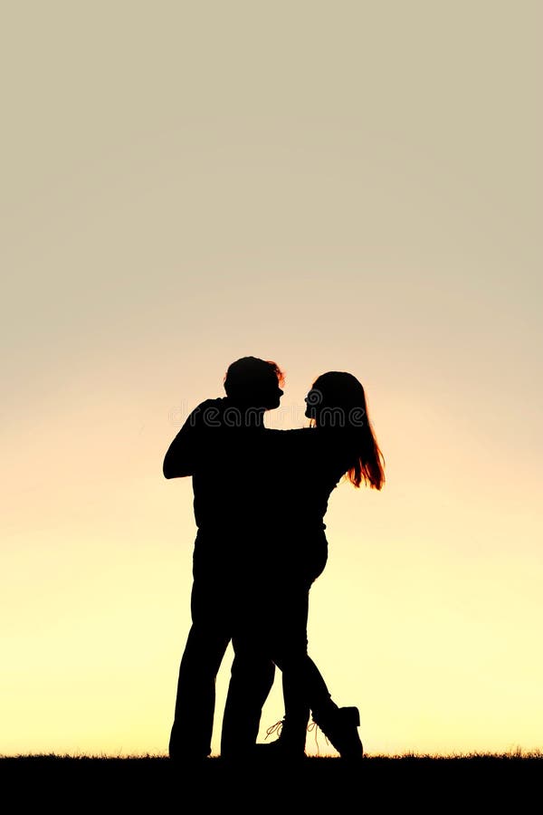 Silhouette d'un jeune couple heureux dansant au coucher du soleil image stock