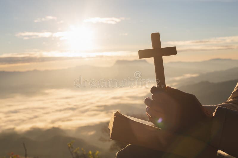 Silhouette de main de femme tenant l'ascenseur saint de la croix chrétienne avec le fond clair de coucher du soleil images stock