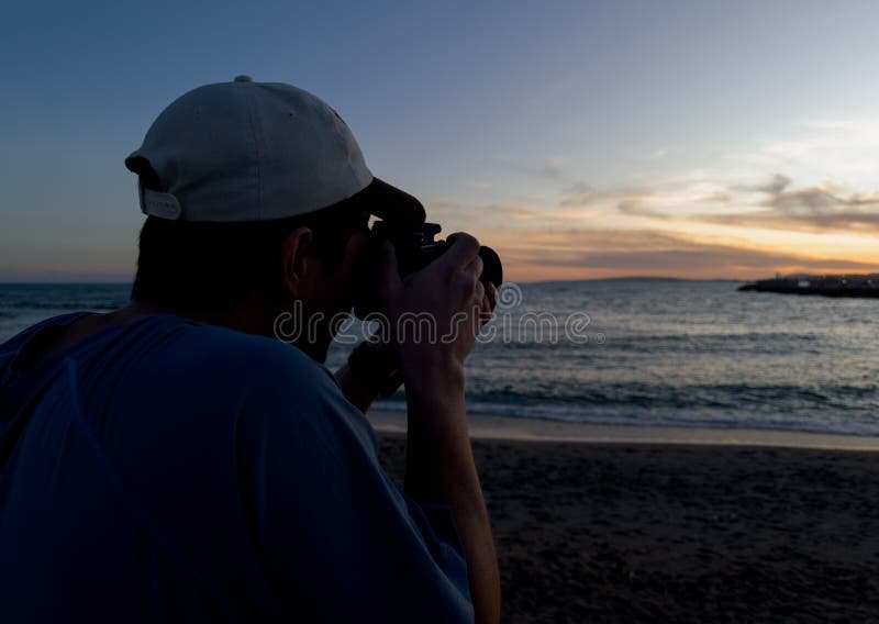 Silhouette de un fotógrafo tomando fotos al atardecer cerca del mar imagen de archivo libre de regalías