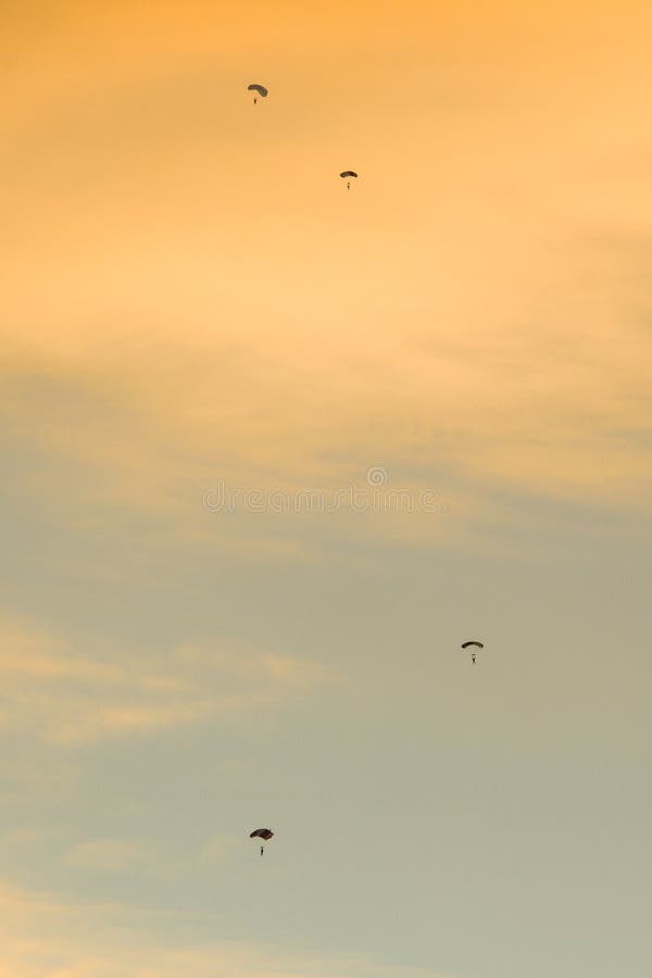 Silhouette des parachutistes volant lentement sur le parachute au coucher du soleil photos stock Silhouette des parachutistes volant lentement sur le parachute au coucher du soleil photos stock