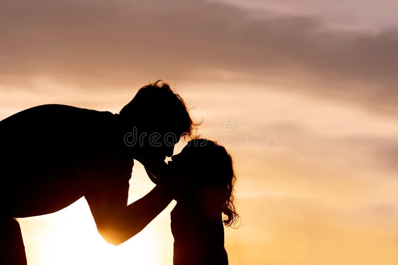 Silhouette di un padre affettuoso che bacia il suo bambino al tramonto fotografia stock libera da diritti