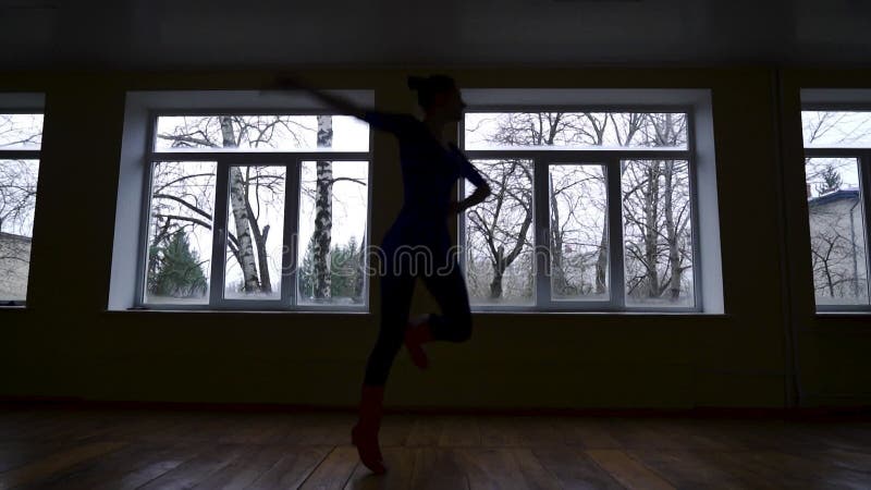 Silhouette di una ballerina che si allena in un'aula buia