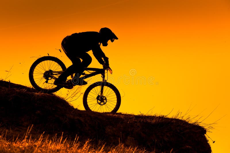 Silhouette of downhill mountain bike rider at sunset