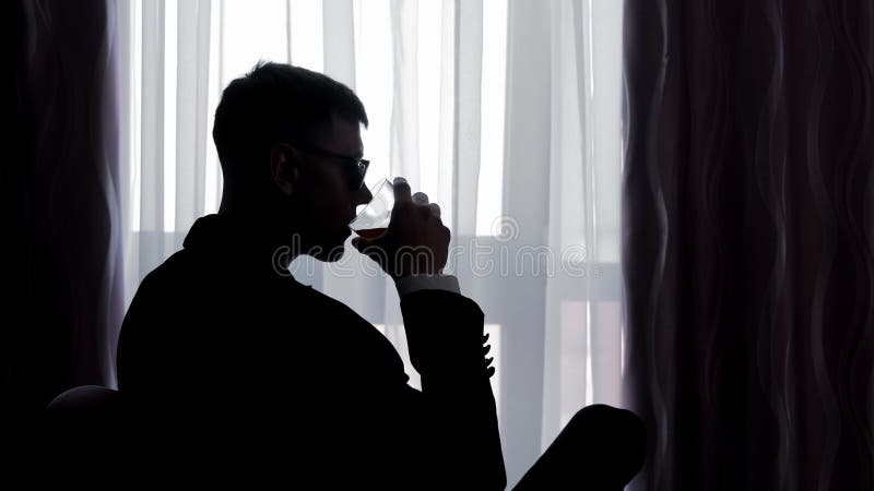 Silhouette du marié tenant à la main un verre par une fenêtre toilette silhouette assise près d'une fenêtre tenant un verre. banque de vidéos