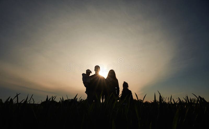 Silhouette einer Frau, die ihre Tochter in Händen hält. ein anderes Mädchen steht und zusieht stockfotografie