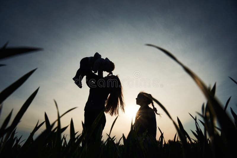 Silhouette einer Frau, die ihre Tochter in Händen hält. ein anderes Mädchen steht und zusieht lizenzfreies stockbild