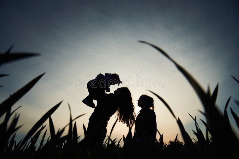 Silhouette einer Frau, die ihre Tochter in Händen hält. ein anderes Mädchen steht und zusieht lizenzfreie stockfotografie