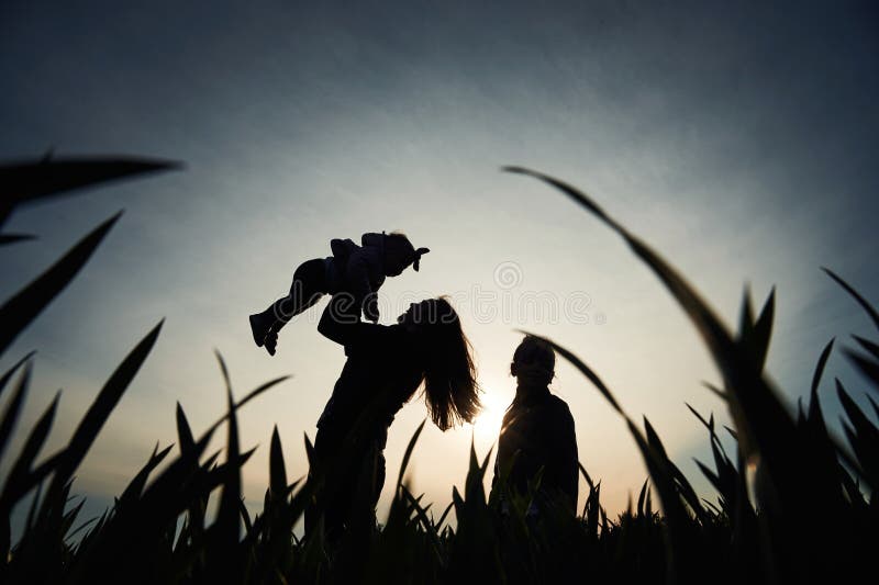 Silhouette einer Frau, die ihre Tochter in Händen hält. ein anderes Mädchen steht und zusieht lizenzfreie stockfotografie