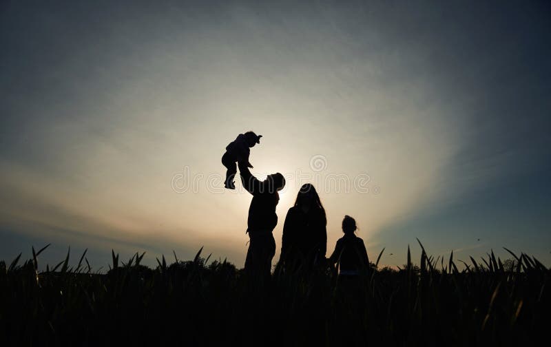 Silhouette einer Frau, die ihre Tochter in Händen hält. ein anderes Mädchen steht und zusieht lizenzfreie stockbilder