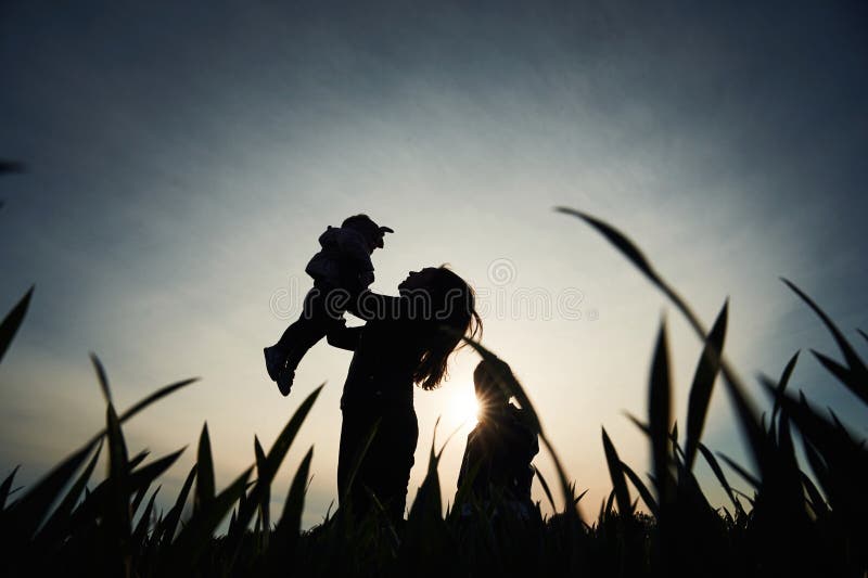 Silhouette einer Frau, die ihre Tochter in Händen hält. ein anderes Mädchen steht und zusieht stockfotos