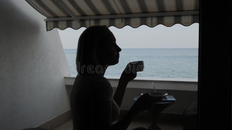 Silhouette einer Frau Kaffee trinken auf dem Balkon eines Hotels mit einem schönen Blick auf das Meer.