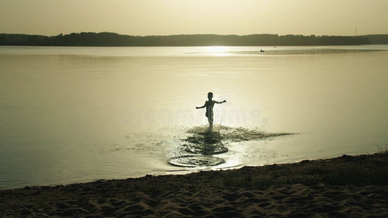 Silhouette eines jungen Jungen, der bei Sonnenuntergang auf einem Sandstrand in den See gelaufen ist