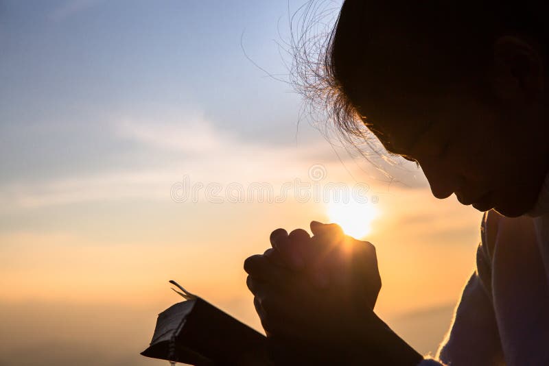 Silhouette, en kristen ung kvinna som ber med ett kors och öppnar bibeln vid soluppgång, en kristen religionskonceptras bakgrund royaltyfri foto