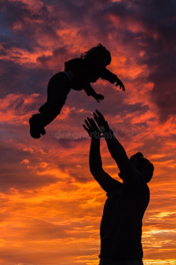 A silhouette of a father playing with his son in the setting sun.