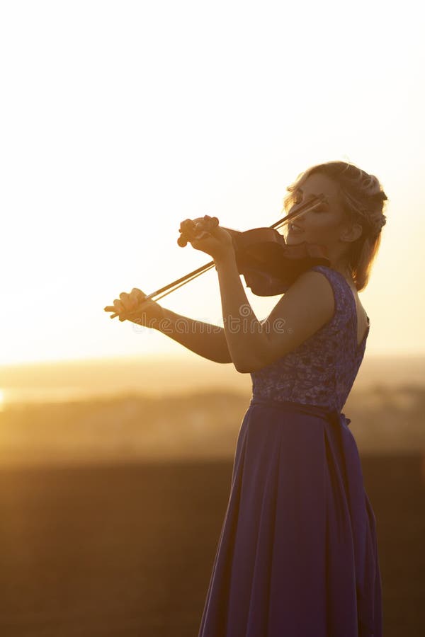Silhouette of a female figure playing the vio and hobbylin at sunset, woman relaxing in music, performance on nature, concept art stock photos Silhouette of a female figure playing the vio and hobbylin at sunset, woman relaxing in music, performance on nature, concept art stock photos