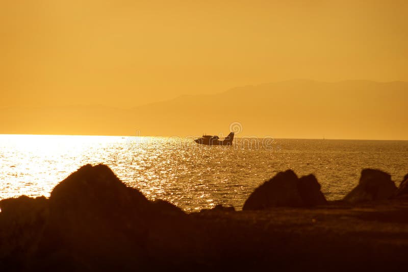 Silhouette of a firefighter plane over the sea, at sunset through the stones stock images