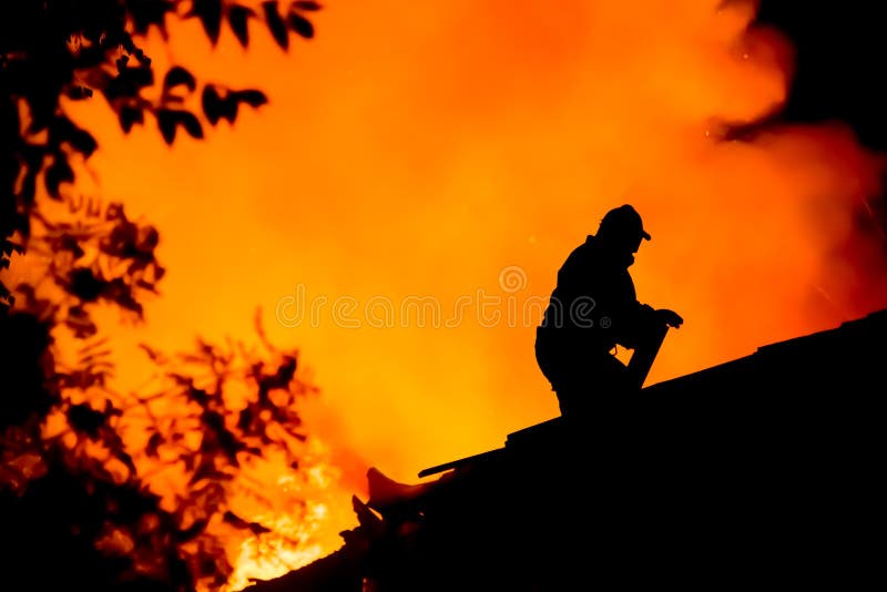 Silhouette of firemen on the roof of a burning house