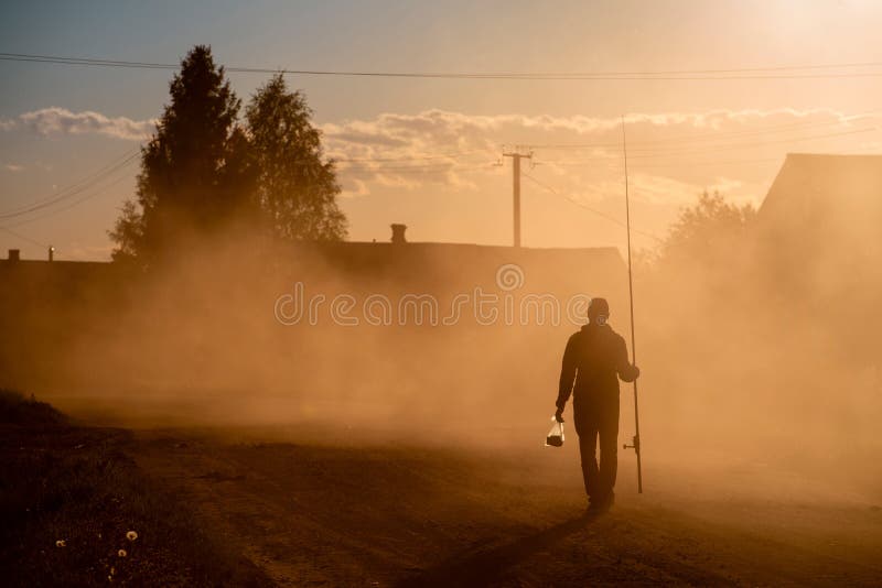 Silhouette of a fisherman walking along a dusty road stock image Silhouette of a fisherman walking along a dusty road stock image