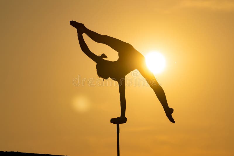 Silhouette of Flexible female circus Artist keep balance on one hand on the rooftop against dramatic sunset. Handstand