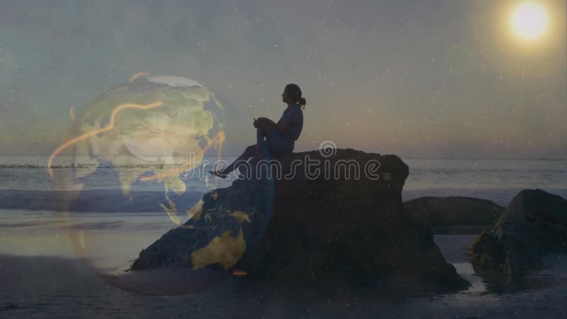 Silhouette féminine assise sur la roche de plage au coucher du soleil montrant globe avec couverture réseau technologique clips vidéos