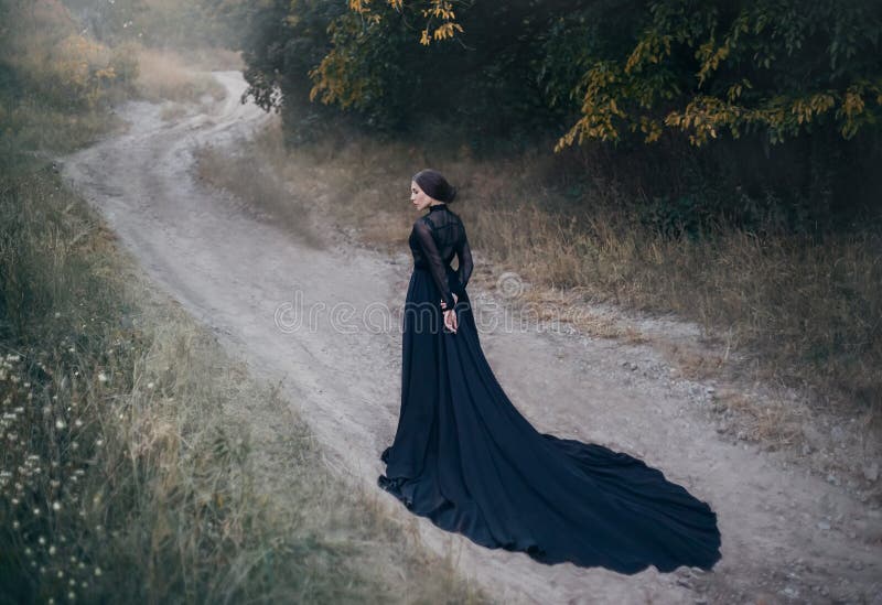 Gothic lady from old horror movie. Walks along the road in the autumn forest.